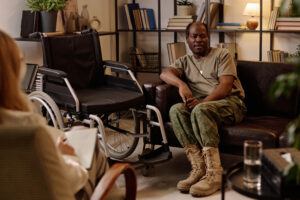 Black veteran with disability sitting on couch in relaxed pose and talking to therapist taking notes